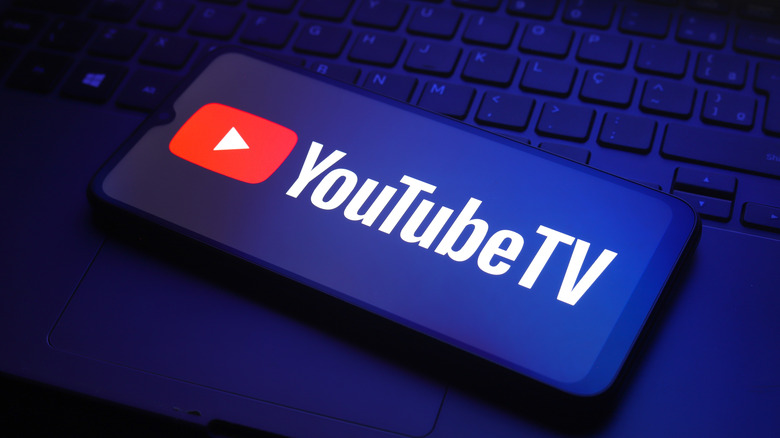 YouTube TV icon in blue hue on smartphone screen with laptop below.