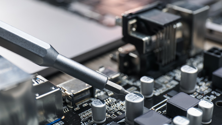Close-up of a screwdriver tip working on a computer motherboard.