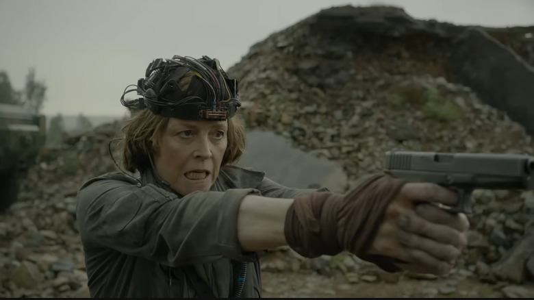 Sigourney Weaver aiming a gun with a computer helmet on her head