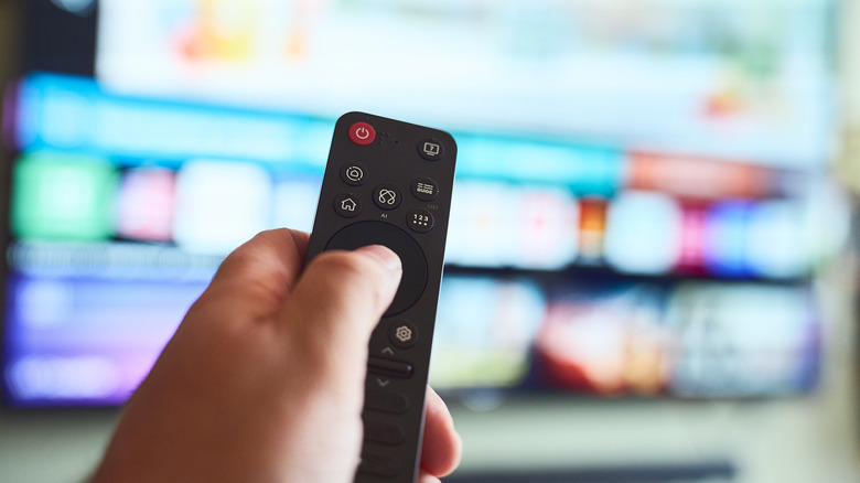 A person pointing a smart TV remote at a blurry TV screen.