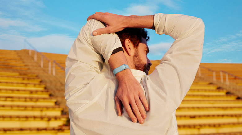 The back of a man in a stadium stretching behind his back while wearing the Fitbit Air.