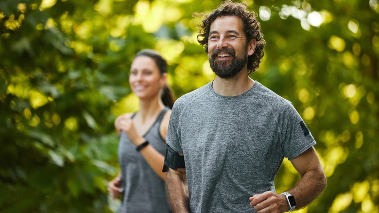 A man and woman running, both wearing fitness trackers on their wrists.