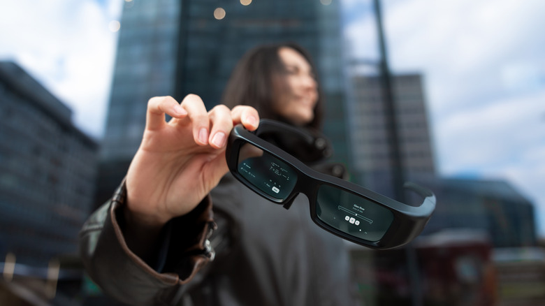 Close up of someone holding smart glasses with screen on in an urban environment.