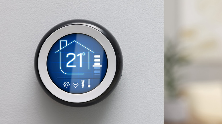 A digital thermostat showing the temperature of the house, placed against a wall
