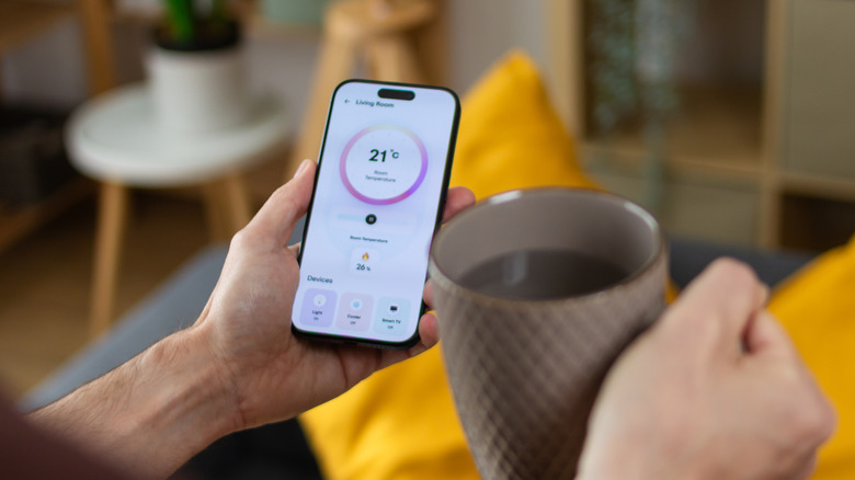 A person checking the smart thermostat app on their phone while holding a coffee mug