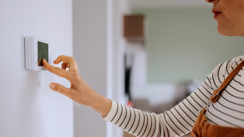 A person operating the smart thermostat placed on the wall of her house