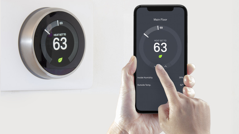 A person using their phone to control the temperature values of a smart thermostat