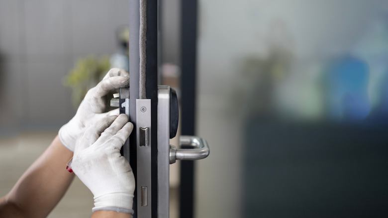 A person performs maintenance on a smart lock that has been installed on a door.