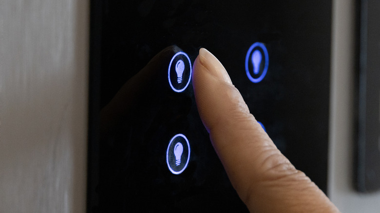 Finger pressing a light button on a wall-mounted smart switch panel.