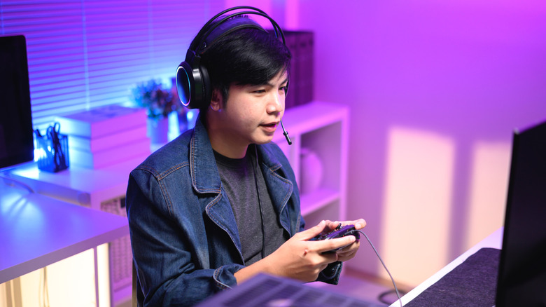 Young man gaming in a room illuminated by purple and blue LED lighting.