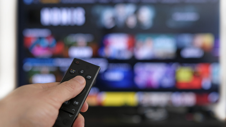 Smart TV blurred in background with hand holding a remote in the foreground.