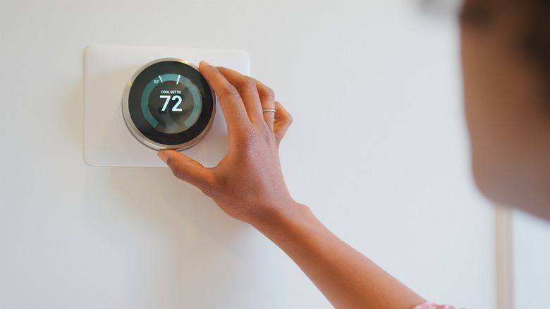A hand adjusting the temperature setting on a smart thermostat