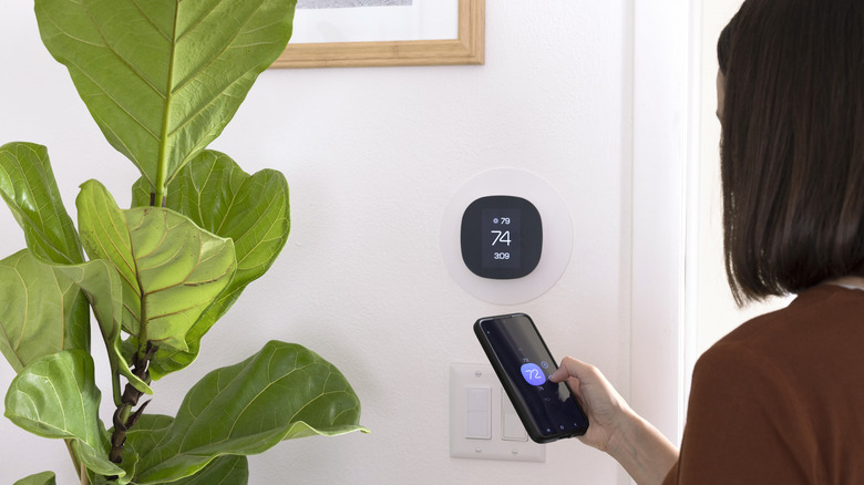 A person using a smartphone app to adjust the temperature setting on a thermostat