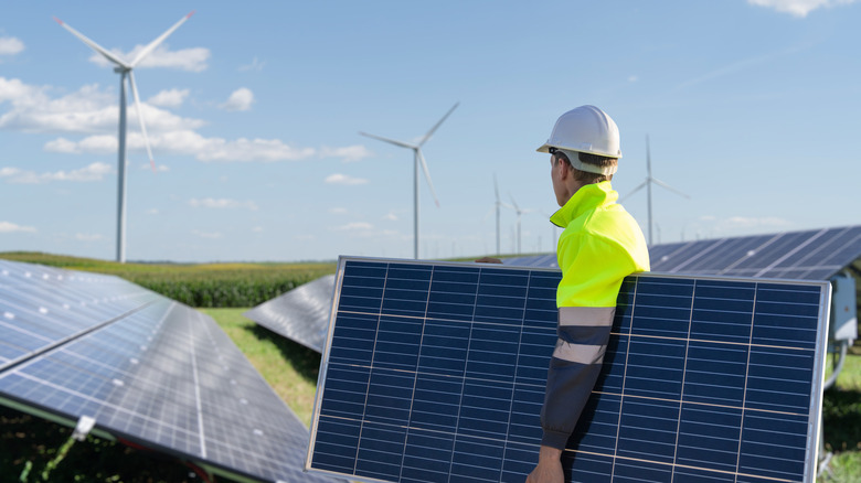 Worker installing solar panels with wind turbines in background