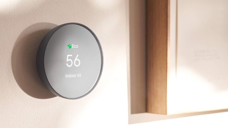 A black Google Nest Smart Thermostat for Home displaying the outdoor and indoor temperatures as it sits connected to a beige wall