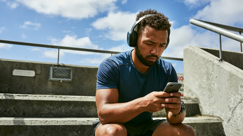man looking at phone in disappointment, headphones on, troubleshooting concept