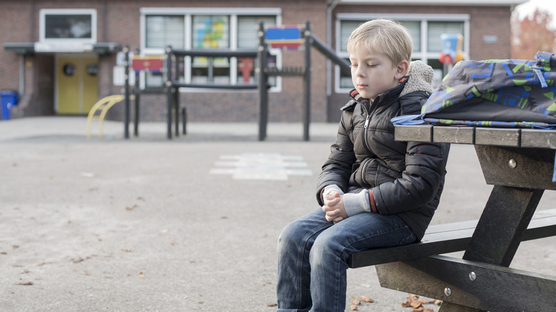 A boy sitting at a bench in a schoolyard