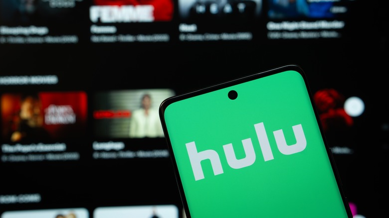 Hulu logo on a mobile device in front of a TV with the streaming service open.