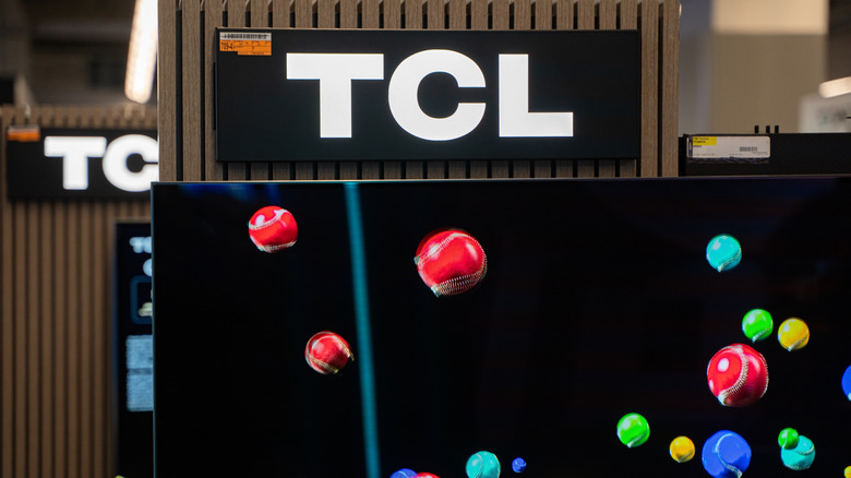 close-up TCL sign over a TV showing multi-colored balls on a black background