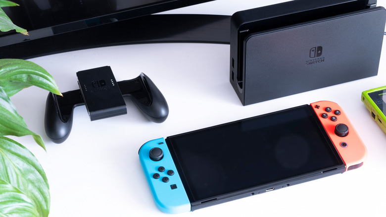 Nintendo Switch LCD with red and blue neon joy-cons and dock on table.