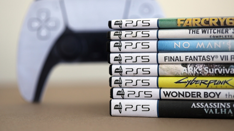 Pile of PlayStation 5 disc cases in front of DualSense controller