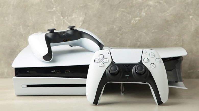PS5 resting horizontally on a table with greyish background and two controllers in the shot