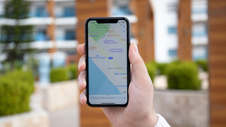 A photograph of a hand holding an iPhone with Apple Maps displayed on the screen.