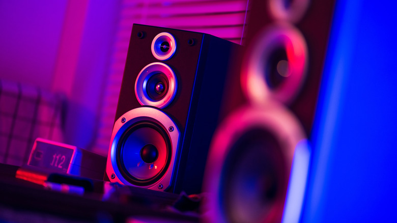 A pair of bookshelf speakers set up in a dark room with ambient RGB lighting.