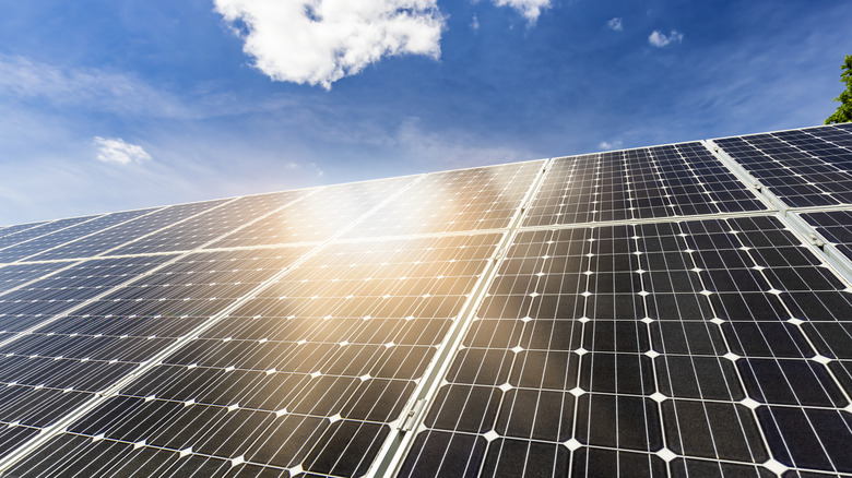 the reflection of the sun on several solar panels, sky and clouds visible in background