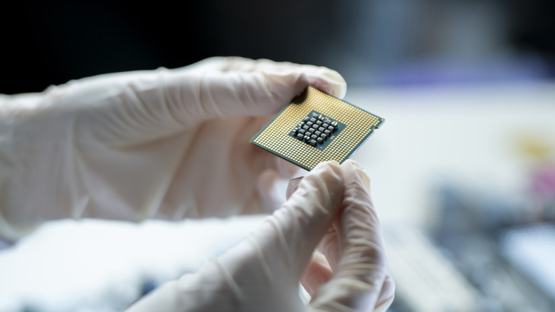Someone wearing gloves holding a computer chip with the bottom exposed.
