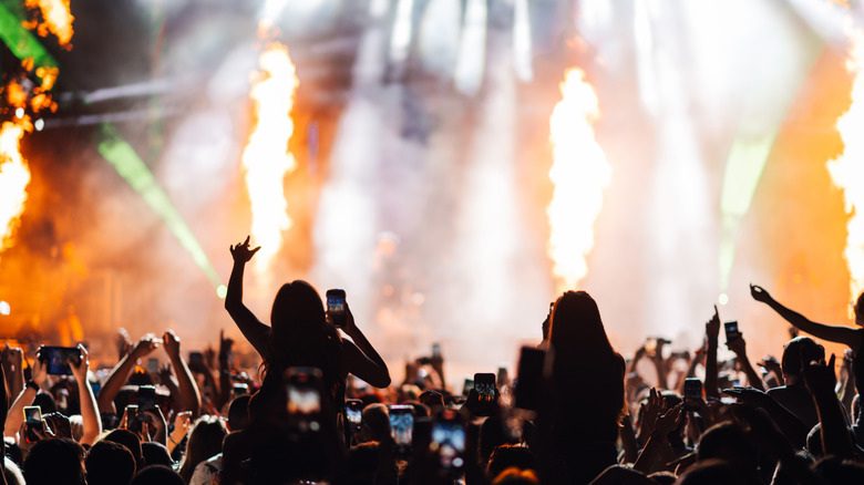 people at a concert, pyro effects, bright lights, large crowd