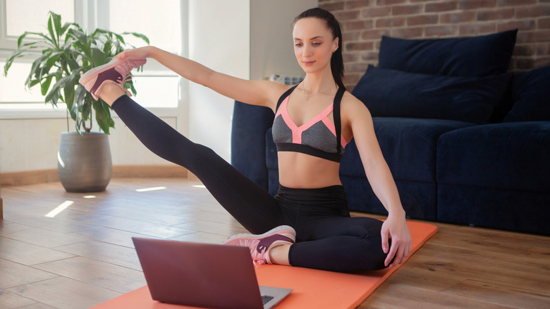 A person working out at home using a laptop to watch fitness videos.