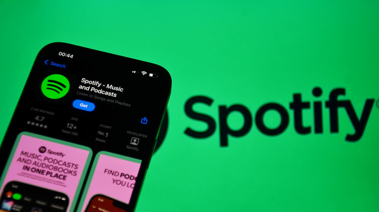 A smartphone displaying the Spotify app in front of the Spotify logo