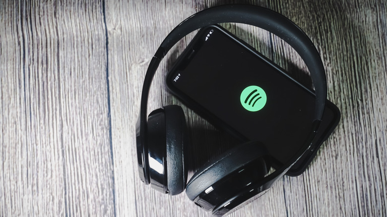 A pair of black over-ear headphones sits atop a black smartphone displaying the Spotify logo