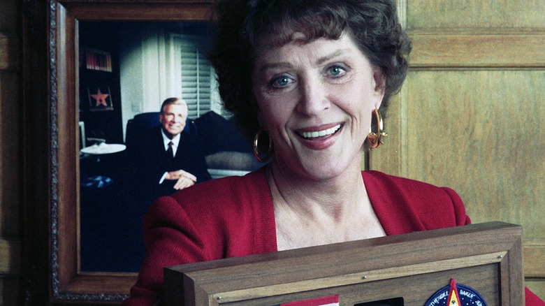 Majel Barrett Roddenberry in front of a photo of Gene Roddenberry.