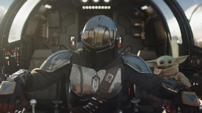 Pedro Pascal acting as the Mandalorian piloting a ship while Grogu stands by his side
