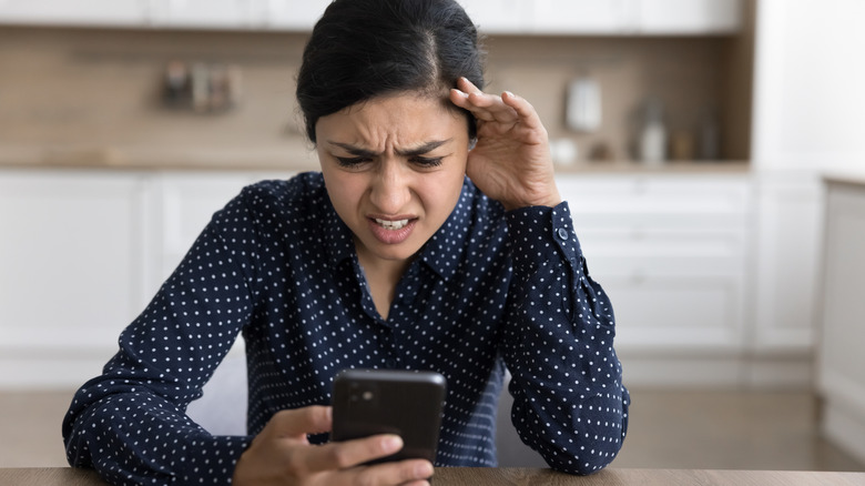 woman outraged looking at her phone in a home setting