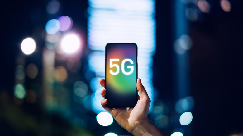 A photo of a hand holding a smartphone with the words 5G on the display.