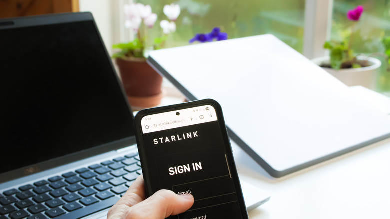 a Starlink Mini internet satellite with a smartphone signing into the Starlink app next to a laptop