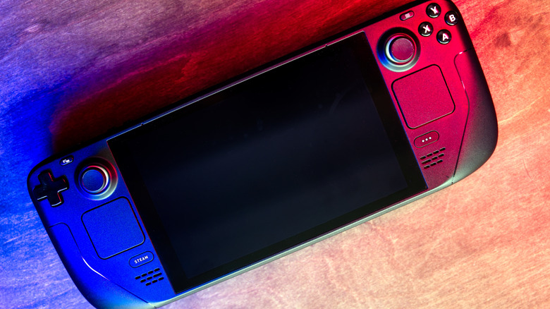 Steam Deck OLED lit by blue and red RGB lighting on a wood tabletop.