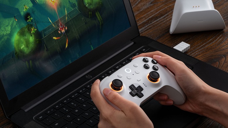 Person playing PC game on laptop with white 8BitDo Ultimate 2 controller