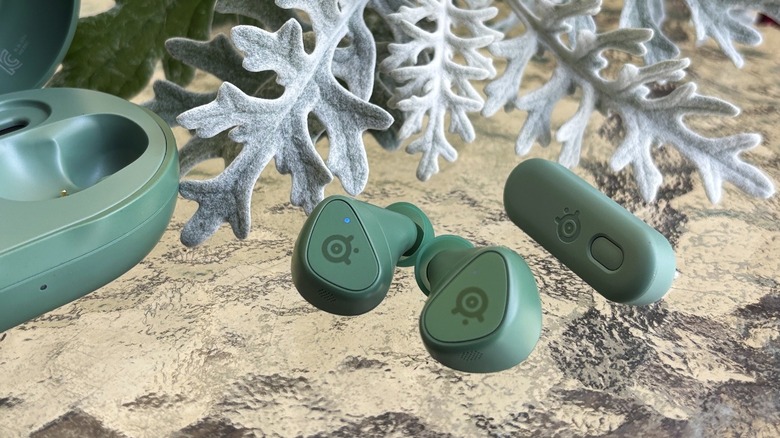 Matcha earbuds with USB-C wireless dongle on glass with white plant in background.