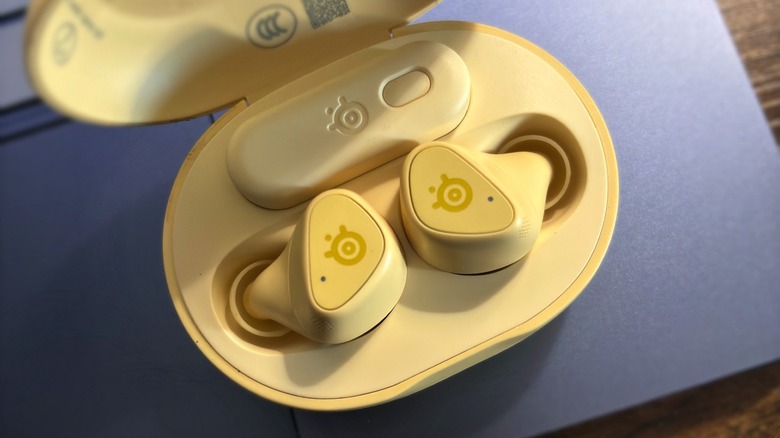 The Arctis GameBuds in the Yuzu colorway sitting on a MacBook palm rest