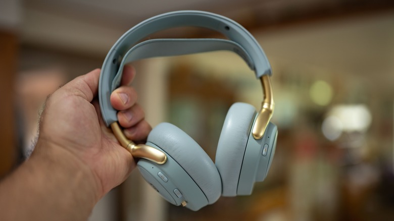 The SteelSeries Arctis Nova Elite held in a hand behind an out of focus room.