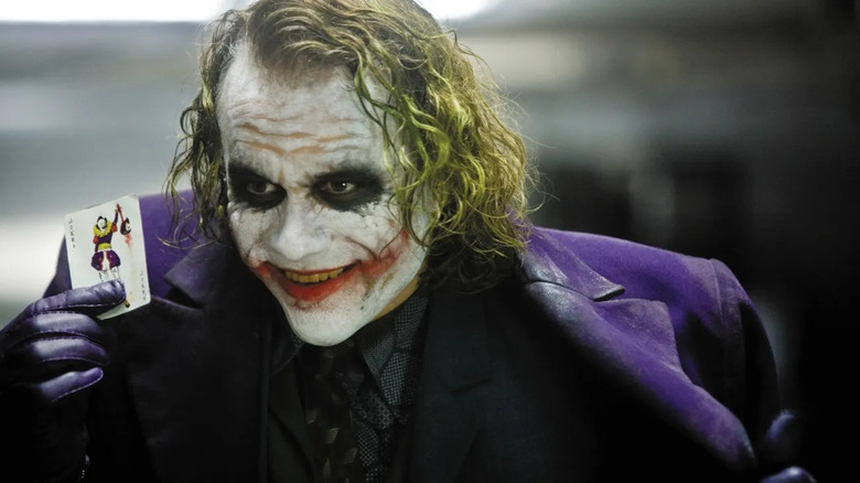 The Joker holding a card and smiling