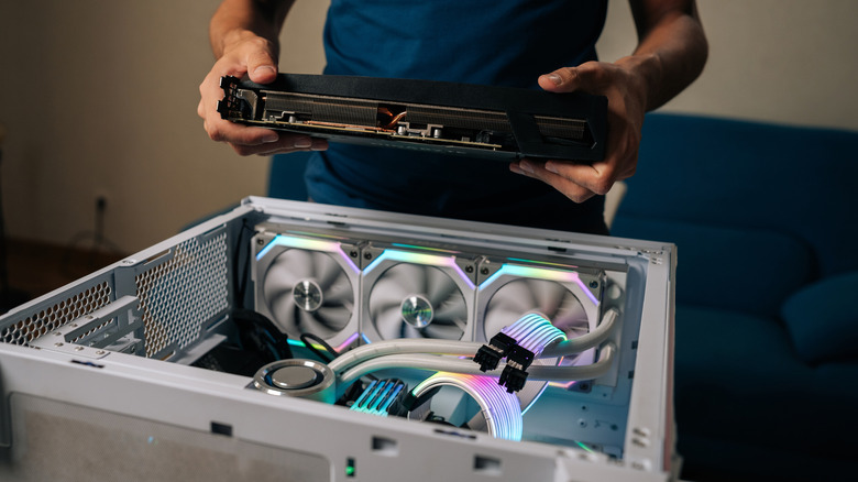 An image of an open desktop PC case with a person holding a detached GPU above it