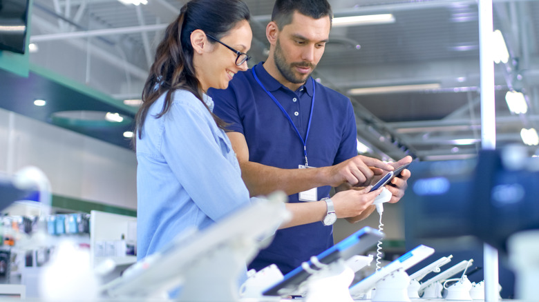 An electronics retail employee assisting a customer with a purchase