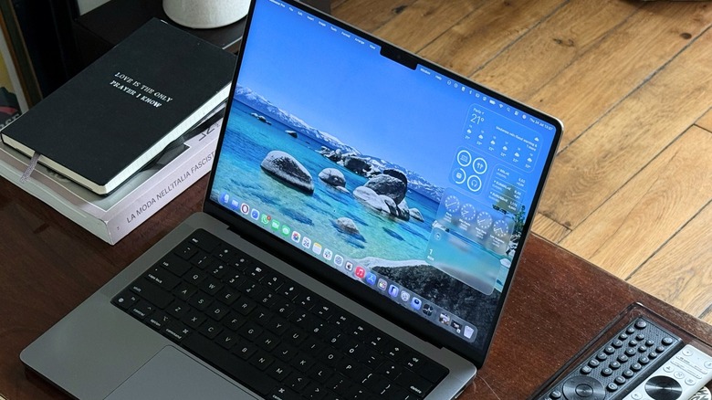 A MacBook Pro on a table with a few books and remote controls around it.