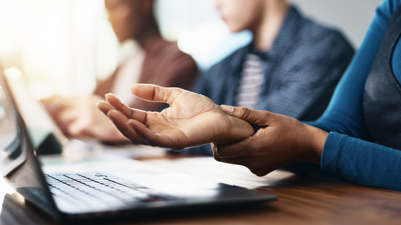 Person at laptop holding wrist due to pain from typing