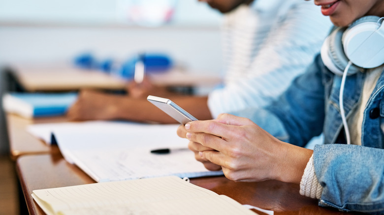 A student uses a smartphone at their classroom desk